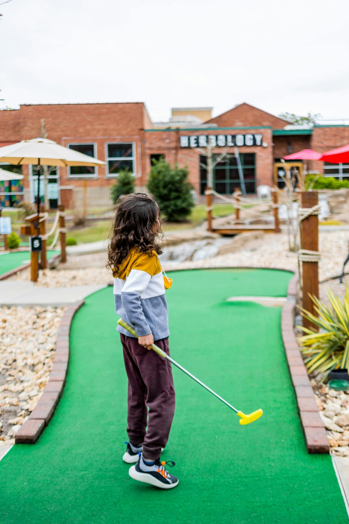 Side view of anonymous child with putter playing mini golf against house facade in city